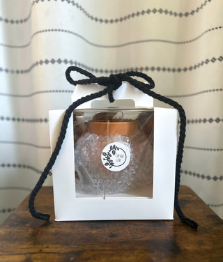 Gift box with a jar inside, tied with a black ribbon, on a wooden surface with a patterned curtain background. Curved leaf logo luxury packing wholesale small business bottom watering self-watering planter and unique handmade gardening gifts minimalist style and coquette kawaii painting made in USA 