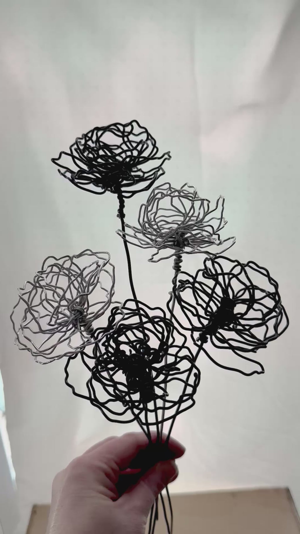 A cluster of three silver wire flowers with intricate, openwork petals. The stems are long and slender, and the flowers are arranged in a bouquet. The background is a solid, dark blue. carnation January birth flower preserved florals Mother’s Day gifts gift for mom silver and black wire flowers delicate pretty decor wedding floral preservation forver flowers wire flower stem carnations curved leaf handmade small business steel aluminum petals dried florals whimsical decor